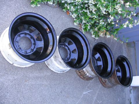 1989 Ford Bronco - A collection of four black rims, some appearing newer than others, are displayed on a concrete surface.