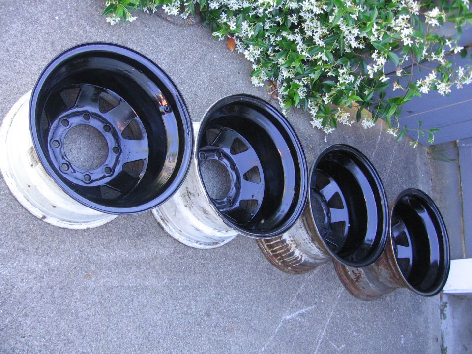 Four black rims of varying sizes laid out on concrete