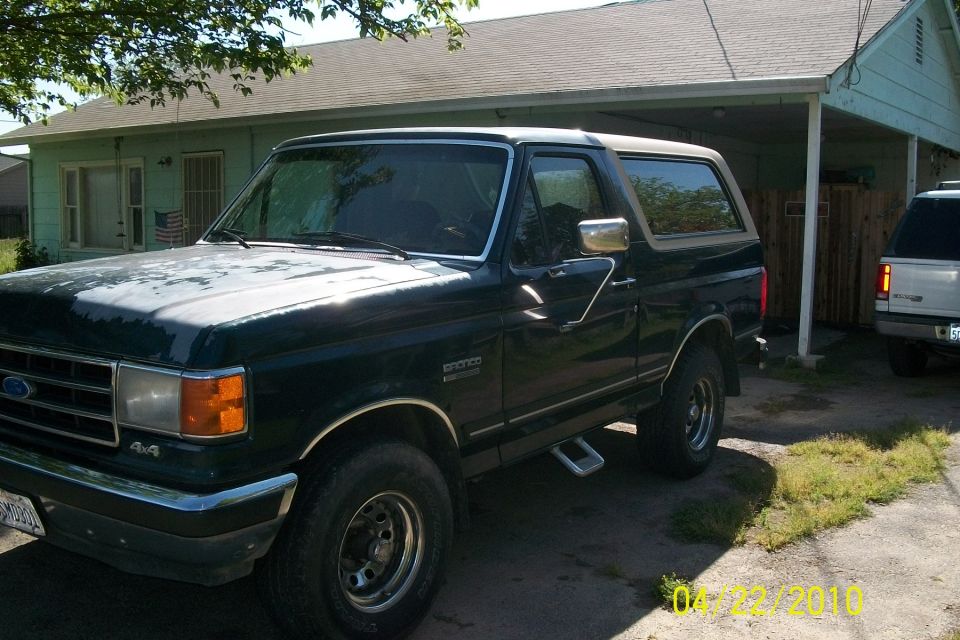 1991 Ford Bronco, dark green, parked in driveway. Another SUV is visible behind it