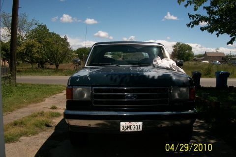1991 Ford Bronco - A dark Ford truck sits parked outside on a sunny day, showing signs of wear on its paint.