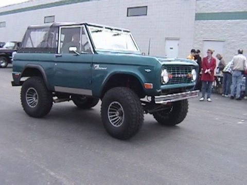 1995 Ford Bronco - A teal Ford Bronco with a black soft top is parked outside a building.