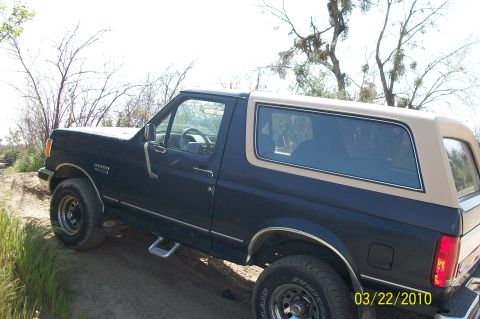 1991 Ford Bronco - This 1991 Ford Bronco is seen on a dirt road with a dark blue body and tan top.