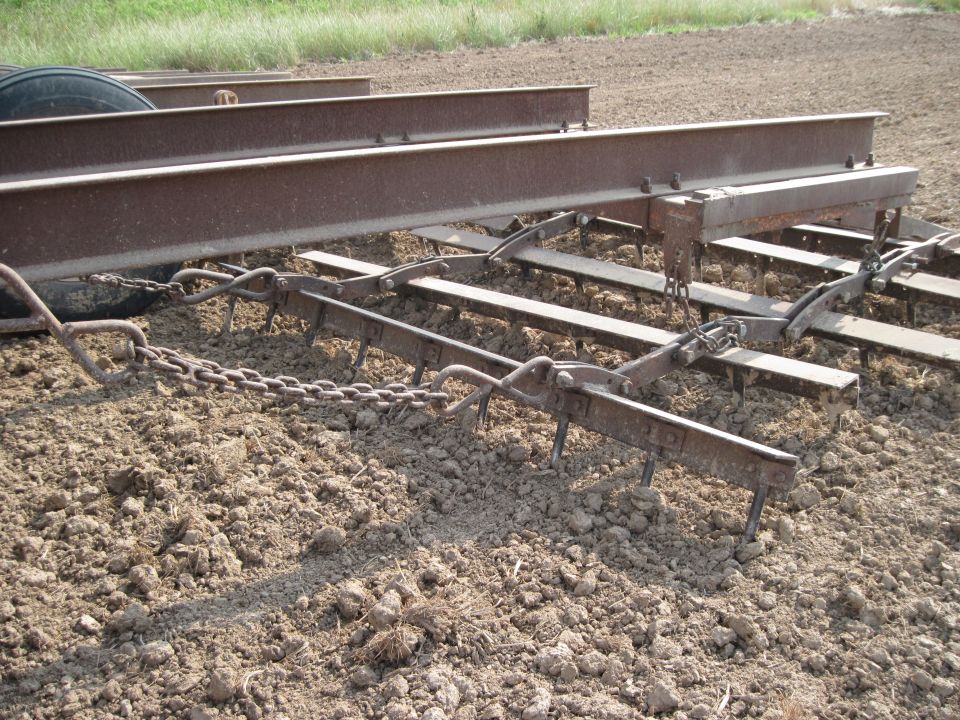 Farm implement with metal beams and tines in dirt field