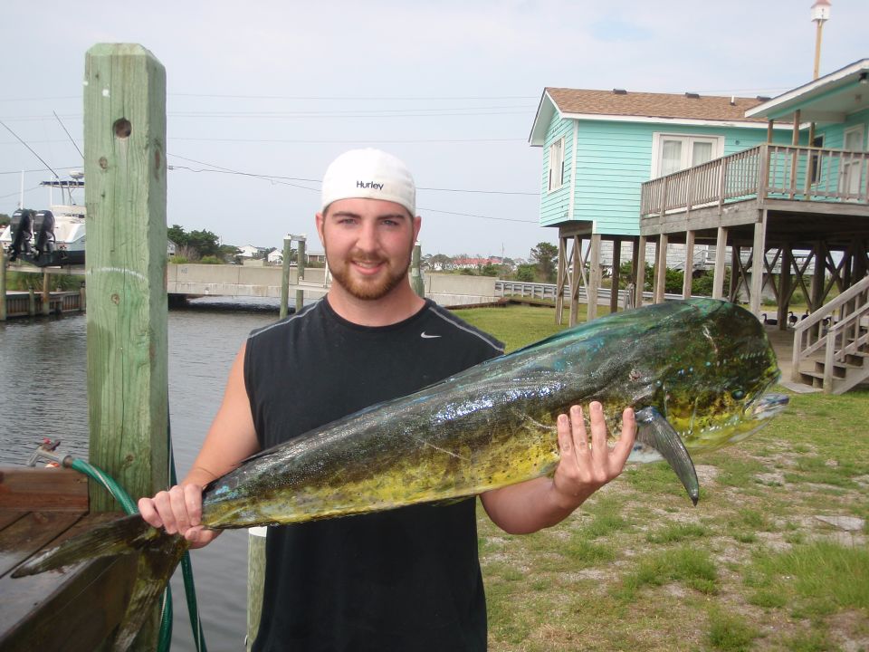 Man holding a large dolphin fish near a house on stilts