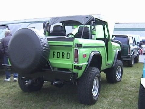 1995 Ford Bronco - Rear view of a green Ford Bronco with a spare tire mounted. Another vehicle is visible behind it.