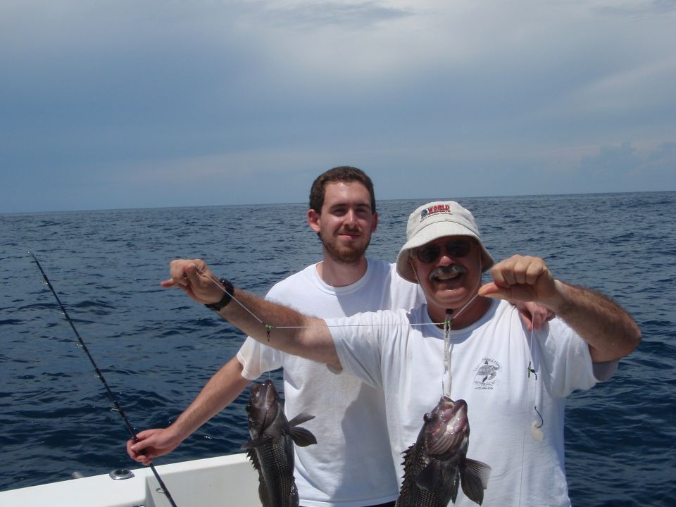 Two men on a boat holding caught fish
