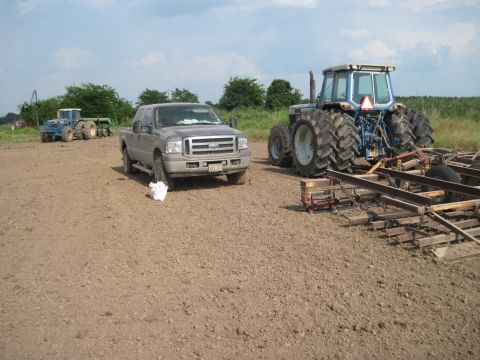 1993 Ford Bronco - Ford pickup truck and two tractors are parked in a dirt field under a cloudy sky.