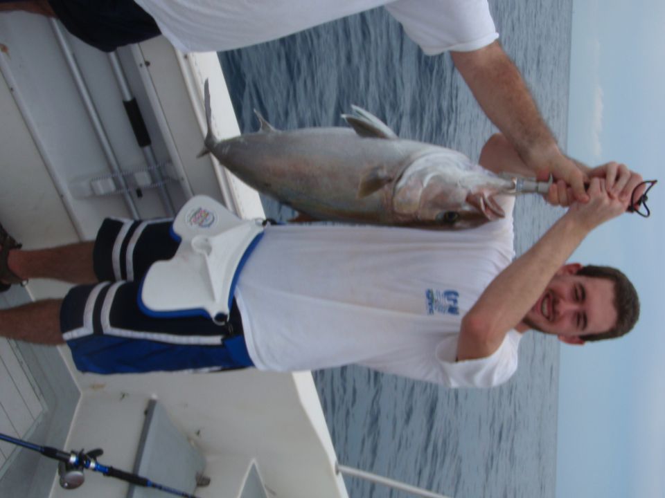 Two guys on a boat holding up a big fish they just caught. One guy is smiling at the camera