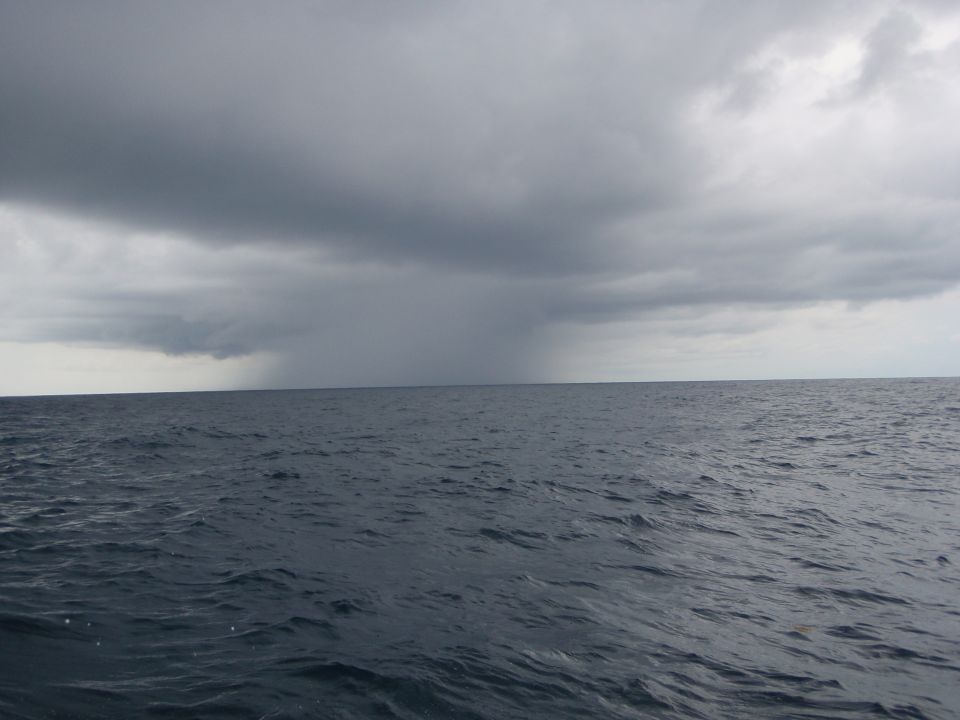 Storm clouds over the ocean with rain falling in the distance. Water shows ripples