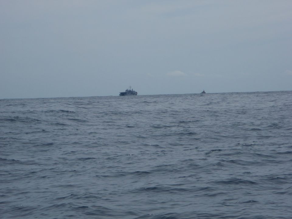 Two ships are visible on the horizon over a choppy sea under a cloudy sky