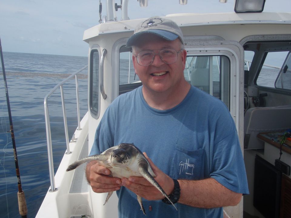 Man holding a sea turtle on a boat with fishing rod