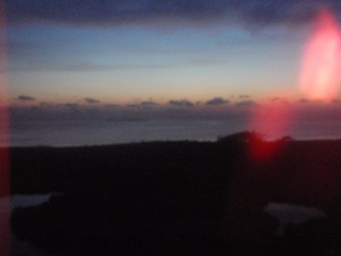 1995 Ford Bronco - A sunset scene over the water, with a dark silhouette of land in the foreground and a red light flare on the right.