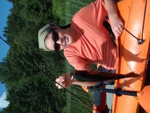 1995 Ford Bronco - A person proudly displays a freshly caught fish while seated in an orange kayak on a body of water, surrounded by lush green trees.