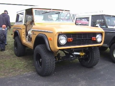 1995 Ford Bronco - A vintage yellow Ford Bronco is shown from the front three-quarter view with its driver's door ajar.