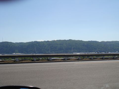 1992 Ford Bronco - A view from a vehicle shows a highway with a distant industrial landscape beyond a wooded hill.