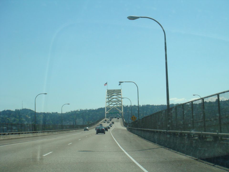 Highway overpass with traffic and a suspension bridge in the distance under a clear blue sky