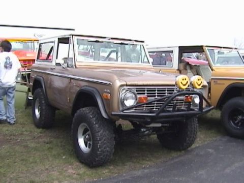 1995 Ford Bronco - This 1970s Ford Bronco features a custom front bumper and unique smiley face auxiliary lights, parked next to another Bronco.