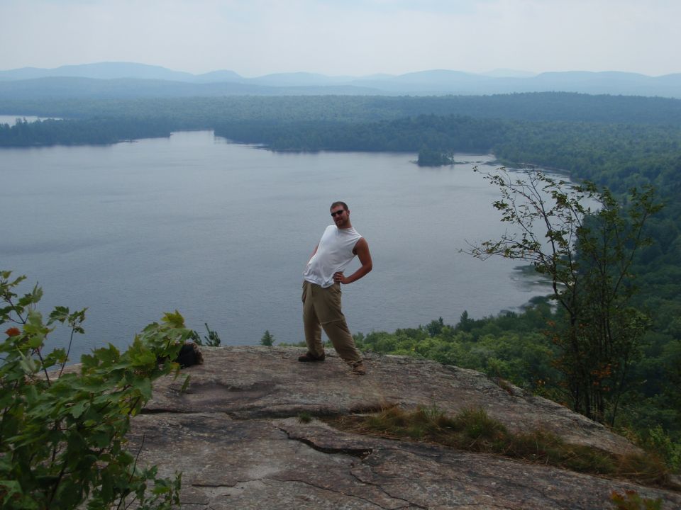 Guy posing on a rock ledge with a lake and trees in the background