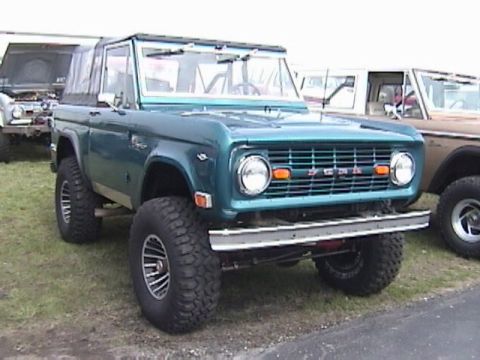 1995 Ford Bronco - This lifted green Ford Bronco is parked outdoors next to another vehicle.