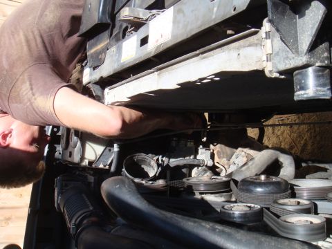 1992 Ford Bronco - A person works on the engine bay of a vehicle, focusing on the radiator and belt system.
