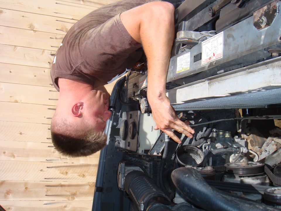 Mechanic working on engine bay, Supermotors.net logo visible