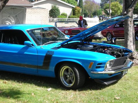 1992 Ford Crown Victoria - A blue 1970 Ford Mustang Boss 302 is displayed with its hood open at a car show, alongside other vehicles.