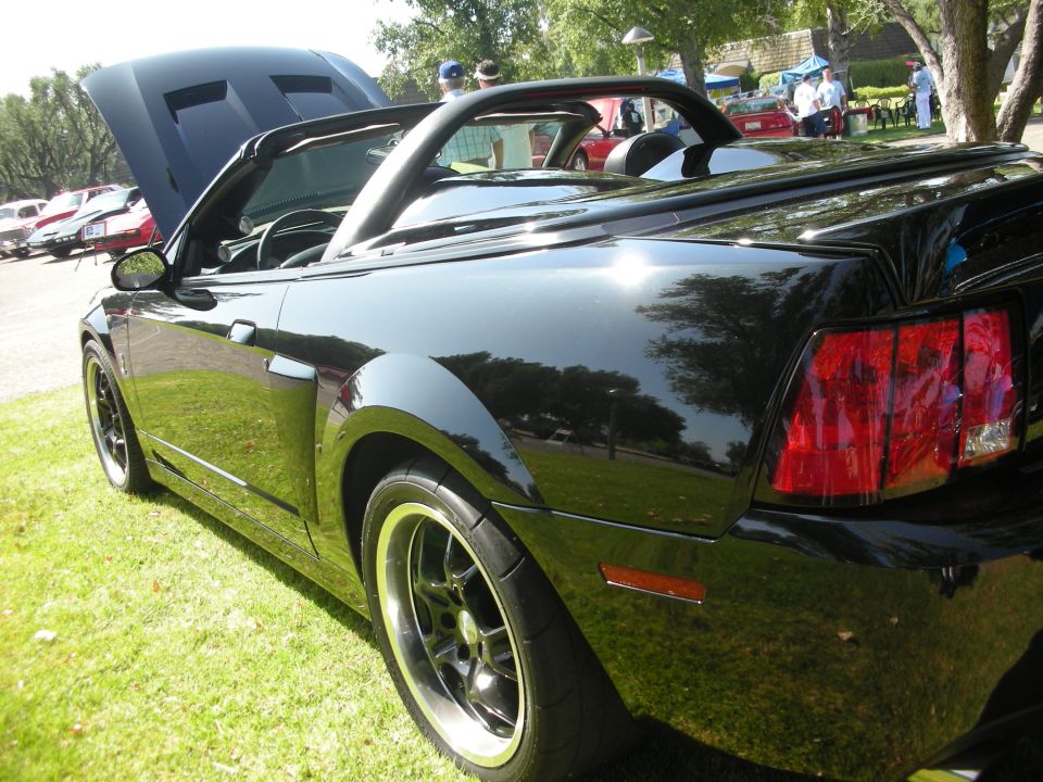 Black convertible sports car with hood open, rear quarter view, on grass
