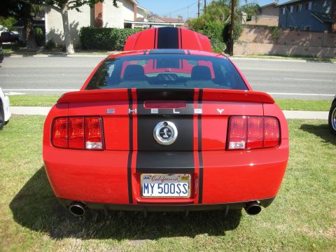 1992 Ford Crown Victoria - A red Ford Mustang with black racing stripes and Shelby badging is parked on grass.