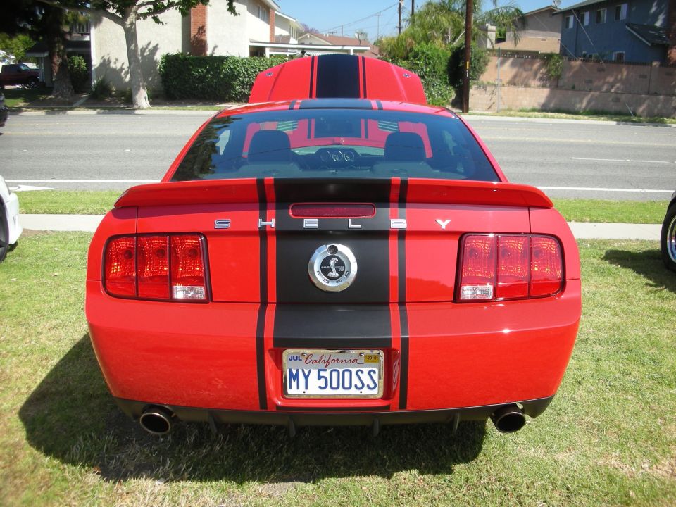 Red Ford Mustang with black racing stripes and Shelby badging, rear view