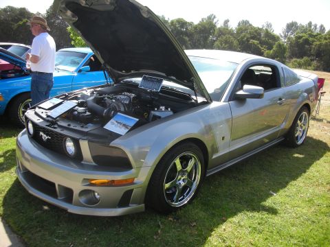 1992 Ford Crown Victoria - A silver Ford Mustang is displayed with its hood open at a car show, revealing a supercharged engine.