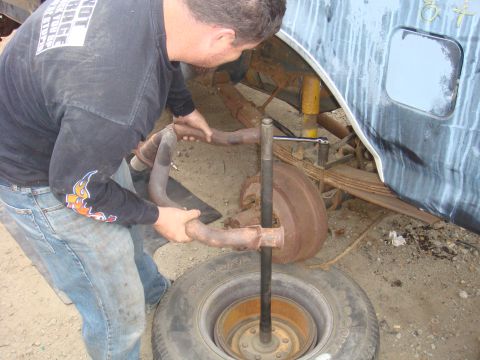 1992 Ford Bronco - Mechanic works on exhaust system components next to a tire and rear suspension.