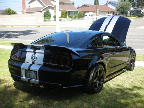 1992 Ford Crown Victoria - Black Ford Mustang with silver racing stripes and louvers on rear window.