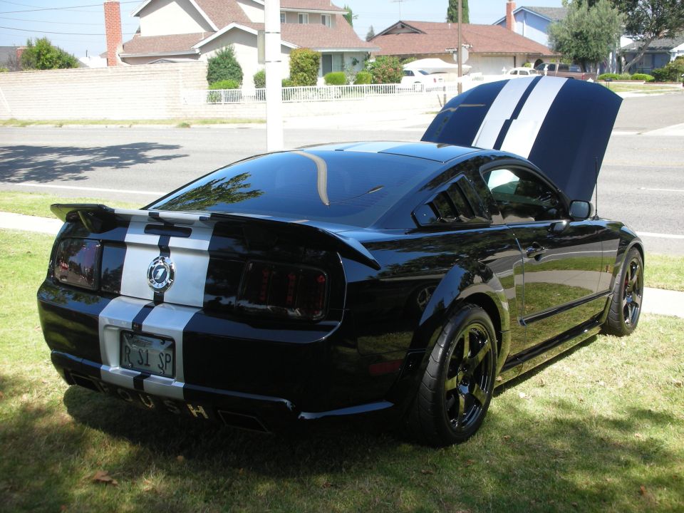 Black Ford Mustang with silver racing stripes, louvers on rear window, and hood open