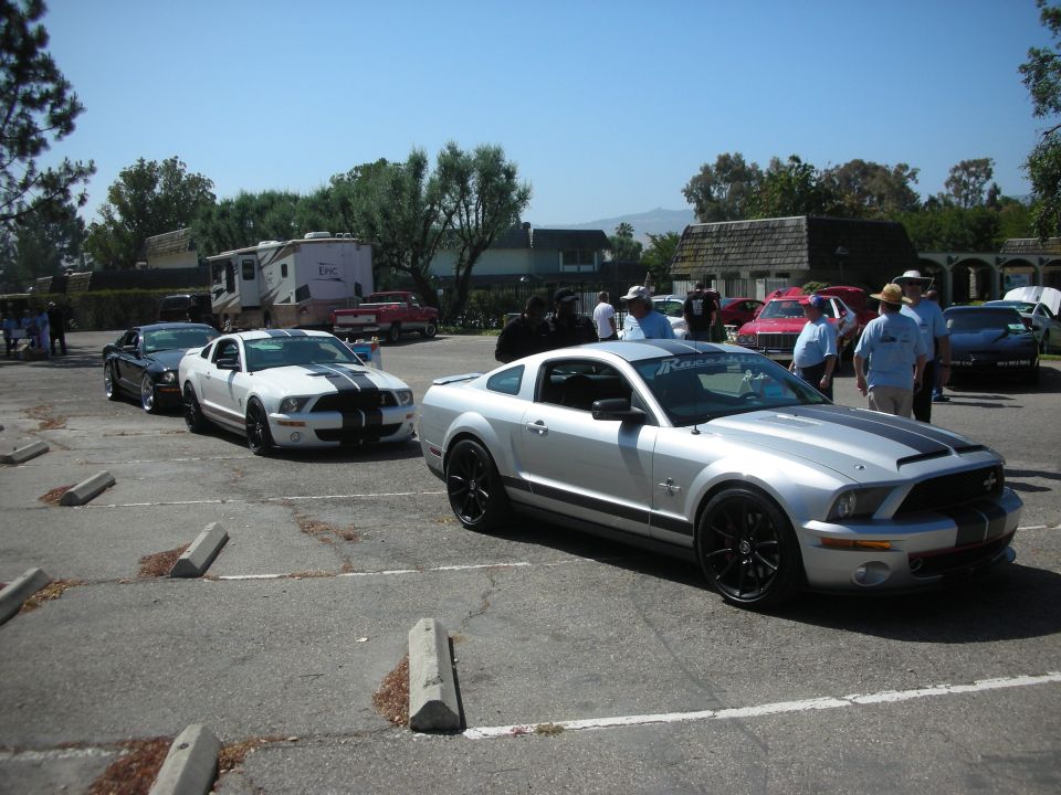Silver Ford Mustang with black stripes parked in a lot with other cars and an RV