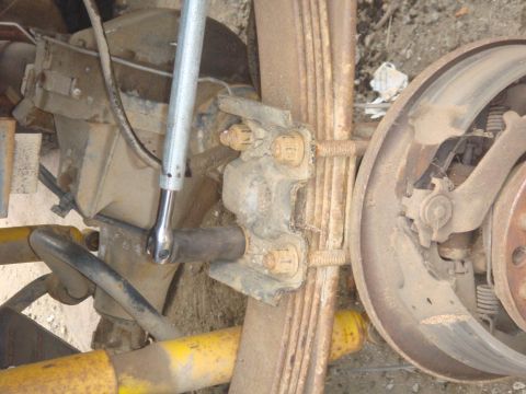 1992 Ford Bronco - Close-up of a rear axle assembly, showing leaf springs, brake drum, and a wrench working on a U-bolt.