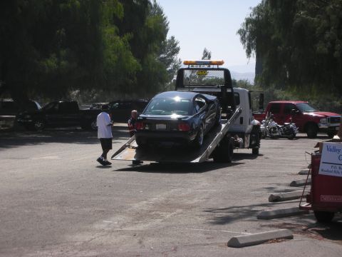 1992 Ford Crown Victoria - A car is loaded onto a tow truck at an outdoor event, with other vehicles visible in the background.
