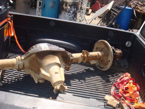 1992 Ford Bronco - A rear axle assembly is transported in the bed of a pickup truck, alongside various discarded items.
