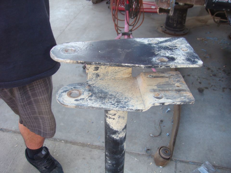 Dirty metal bracket assembly with bolt holes, held by a black pipe