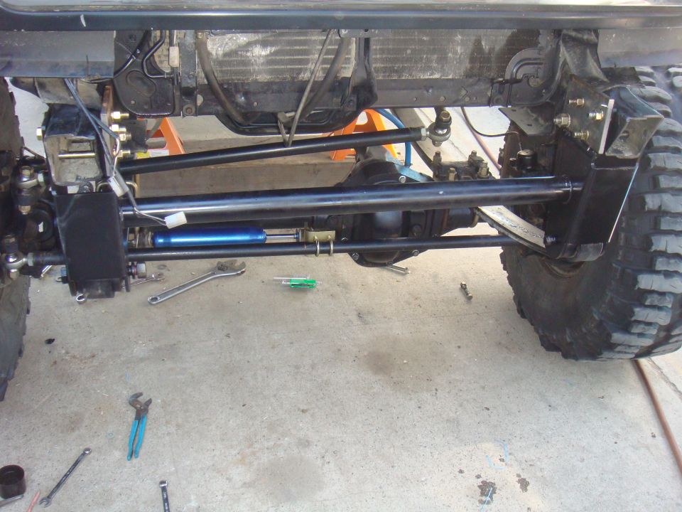 Vehicle undercarriage with large tires, suspension linkages, and a blue steering stabilizer