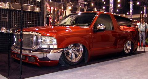 1995 Ford Bronco - This heavily modified Ford Excursion SUV is displayed at an indoor event with custom chrome wheels and a lowered stance.