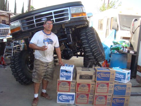 1992 Ford Bronco - A man stands with a stack of beer boxes next to a custom lifted Ford truck, with another truck visible in the background.