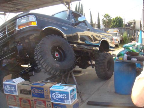 1992 Ford Bronco - A heavily modified 1992 Ford Bronco is shown on jack stands, with a stack of beer boxes nearby.