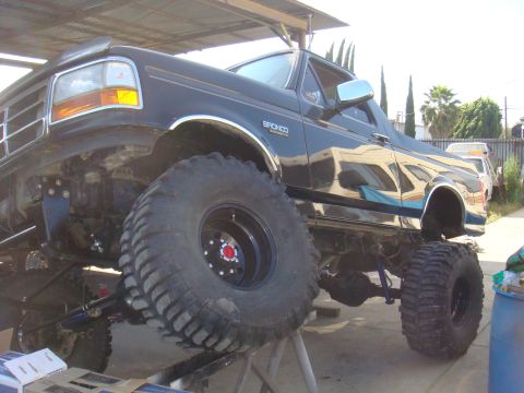 1992 Ford Bronco - A black 1992 Ford Bronco is shown with its suspension and large tires, indicating it is undergoing modifications.