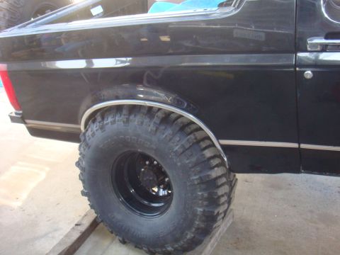 1992 Ford Bronco - Close-up of a large tire and fender on a black SUV, with a watermark for Supermotors.net.