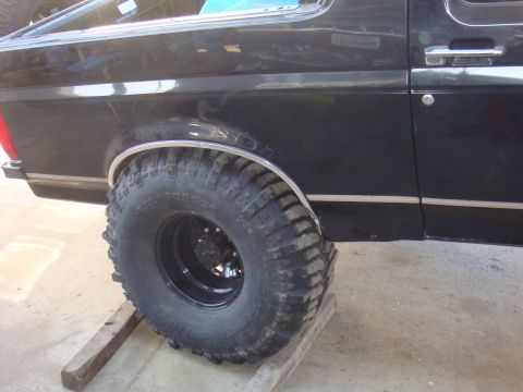 1992 Ford Bronco - The rear quarter panel and large off-road tire of a black 1992 Ford Bronco are visible.