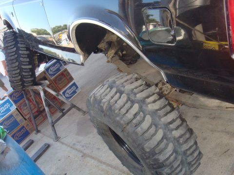 1992 Ford Bronco - A black SUV's rear fender and massive off-road tire are visible, supported by stands and cases of Bud Light.