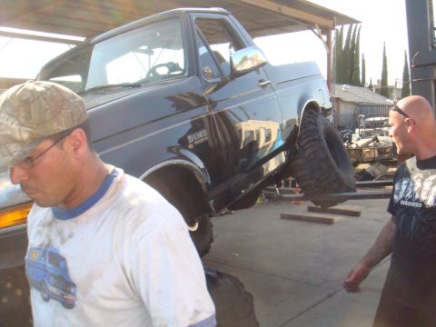 1992 Ford Bronco - A black 1992 Ford Bronco is elevated on a rack, with two men observing the work.