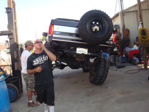 1992 Ford Bronco - A lifted Ford truck is being worked on in a garage with two men present.
