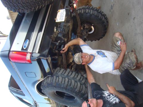 1992 Ford Bronco - Two men work on the rear axle of a 1992 Ford Bronco, with a visible license plate.