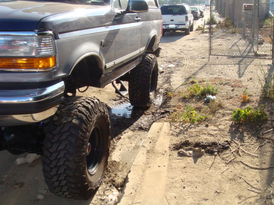 Dark gray 1992 Ford Bronco with large off-road tires, lifted suspension, parked on dirt